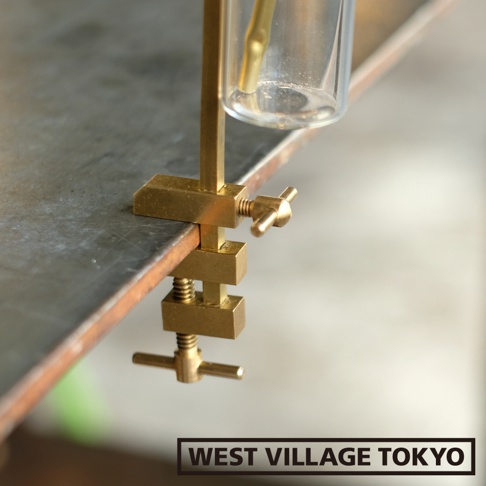 黃銅可夾式玻璃線香架，夾具主體為黃銅材質，帶有兩個旋轉螺絲，用於固定在桌邊。上方夾持著一個透明玻璃管，管內有少量液體和一根黃銅管。