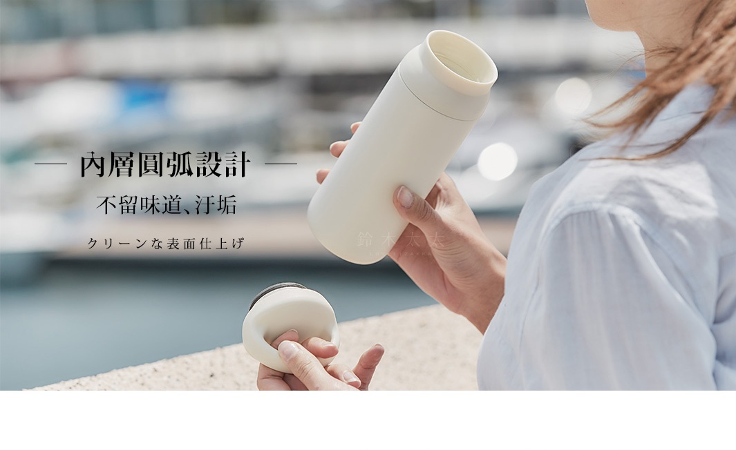 米白色提式輕巧保溫瓶，瓶身圓潤，搭配同色系瓶蓋，由女性手持，背景為模糊的戶外景觀。