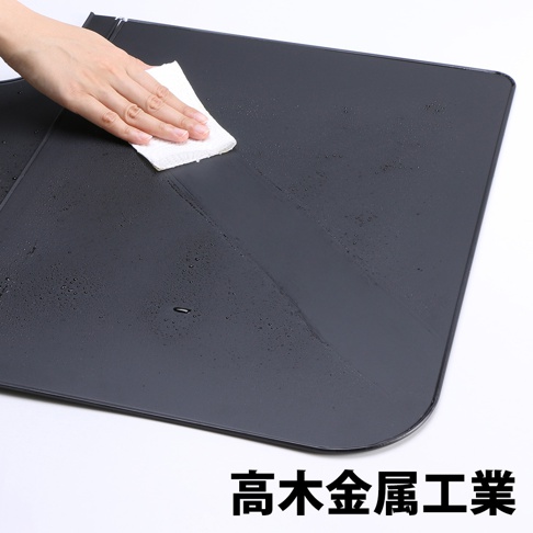 深灰色 L 型折疊擋油板，表面有水珠，一隻手正用白色紙巾擦拭。