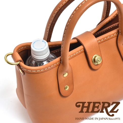 職人手作皮革迷你托特包，呈現原色皮革的溫潤質感，包身簡潔，配有提把與金屬釦，內部可見一瓶礦泉水。