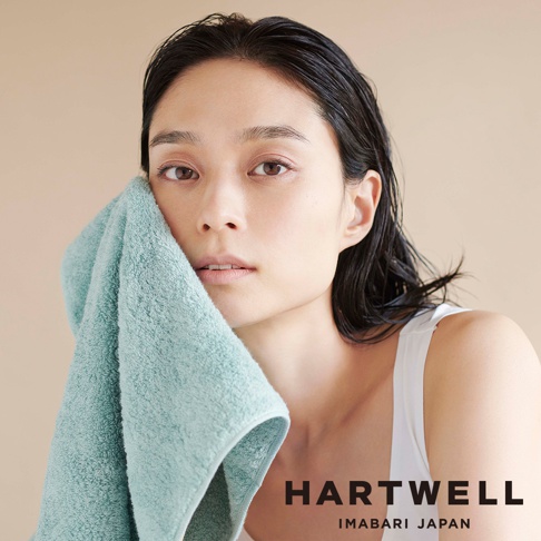 一位女性用淺藍色柔軟毛巾輕柔擦拭臉部，展現肌膚質感。