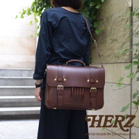 一名女子斜背著一個深棕色皮革製的歐式三用學生包，包包上有兩個皮帶扣和金屬釦，提把和背帶皆為皮革材質。