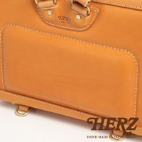 職人手作皮革橫式書包，特寫細節，呈現天然皮革紋理與精緻縫線，上方有HERZ品牌標誌，下方有HAND MADE IN JAPAN Since1973字樣。