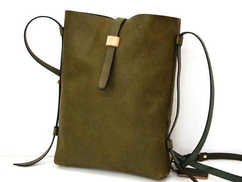 職人手作皮革散步直式單肩包，採用質感的綠色皮革製成，設計簡約，帶有可調節的肩帶和一個小巧的卡其色皮革繫帶，整體呈現休閒而實用的風格。