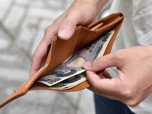 職人手作皮革三折式迷你短夾，展示著淺棕色皮革材質，夾內有日圓鈔票。