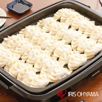 黑色烤網風電烤盤 APA-136 鋪滿了整齊排列的生水餃，烤盤邊緣可見 IRIS OHYAMA 品牌標誌。