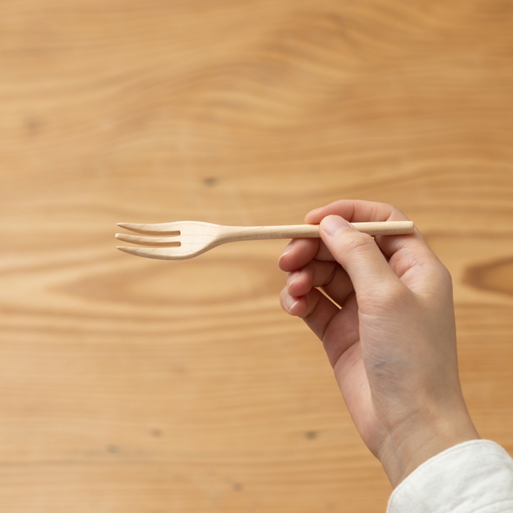 手持一枝淺色楓木製作的點心叉，叉身帶有自然的木紋。