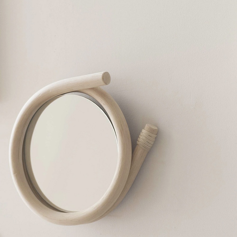 一個帶有天然藤編框架的圓形鏡子，框架呈彎曲的螺旋狀，一端有編織紋飾，整體呈現淺木色調。