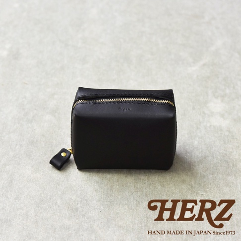 黑色皮革箱型收納包，正面有燙金Logo，配有金色拉鍊及同色皮革拉環，包包下方印有HERZ品牌字樣。