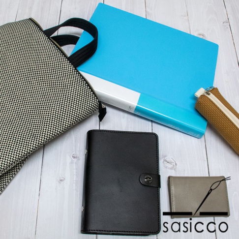 黑白棋盤格紋帆布手提後背包，搭配一個藍色文件夾、一個棕色筆袋、一個黑色皮質記事本和一個灰色卡夾。