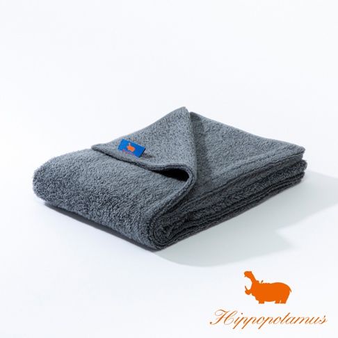 深灰色竹棉混紡厚實大浴巾，表面有柔軟絨毛，一角縫有藍色標籤，印有橘色河馬圖案。