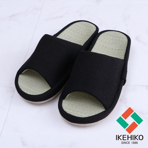 一雙黑色的藺草透氣室內拖鞋，鞋面為織物材質，鞋墊為藺草編織，呈現天然的淺綠色，拖鞋開口設計，適合居家穿著。
