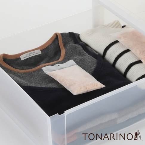 透明材質包裝內的淺褐色顆粒，置於衣物抽屜中，與深灰色、藍色及黑白條紋針織衫一同擺放。