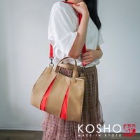 淺褐色棉帆布製成的扇形托特包，飾有鮮紅色拼接，可肩背或手提，附有紅色肩帶。