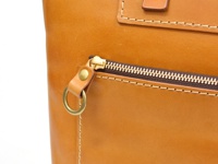 職人手作皮革威靈頓直式拉鍊托特包 (T-151)，特寫展示包款的淺棕色皮革表面，包括一個帶有黃銅拉鍊頭和圓形掛環的拉鍊口袋，以及精緻的縫線細節。