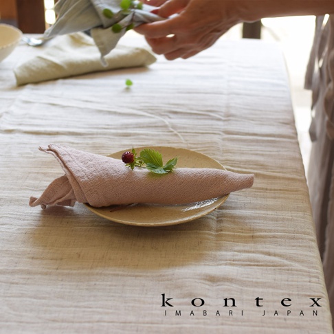 淺粉色輕柔紗布巾捲成一團，放在淺盤上，上面裝飾著一顆小草莓和幾片綠葉。