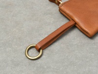 職人手作的棕色皮革鑰匙包，配有黃銅色金屬環和皮革掛繩，展現細緻的縫線與皮革紋理。