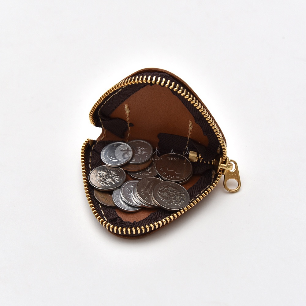 一個深棕色的職人手作皮革三角飯糰造型零錢包，拉鍊呈現半開狀態，內部裝有多枚日本硬幣，中央印有鈴木商標字樣，整體呈現簡約精緻的質感。