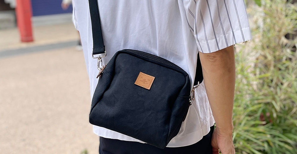 一個斜挎著深藍色石洗帆布散步包的側面鏡頭，包上有一個方形的皮質標籤。