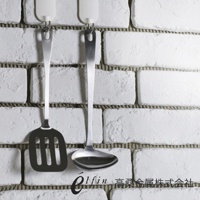 一組日製不鏽鋼廚具，包含一個帶有長柄和圓形湯勺的湯杓，以及一個帶有長柄和方形濾網的鍋鏟，兩者皆掛在白色磚牆上。