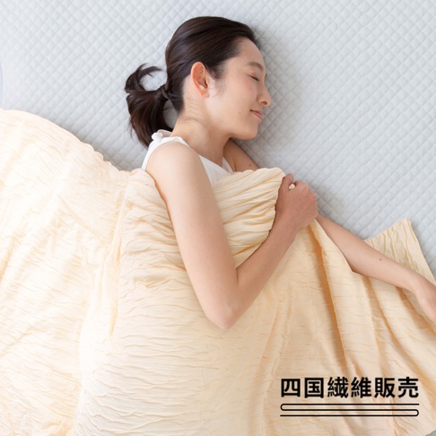 一位女性仰臥，蓋著一條淡黃色、帶有皺褶紋理的舒芙蕾透氣涼被（無棉款）。