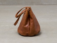棕色皮革抽繩包，帶有可調整的肩背/手提帶，包身呈現圓潤的桶狀，底部有縫線細節。