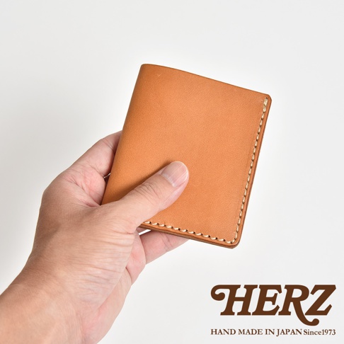 一只手拿著一個品牌為HERZ的日本手工皮革製作的淺棕色兩折式卡片鈔票夾。
