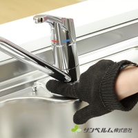 一隻黑色的針織清潔手套，戴在手上，正在擦拭不鏽鋼水槽。手套有指縫設計，材質表面有細小的網紋，手腕處有鬆緊帶。背景是閃亮的水龍頭和水槽邊緣。