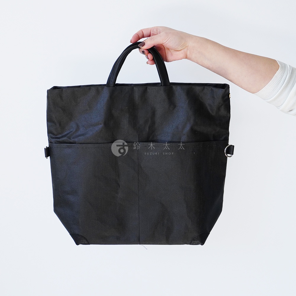 一個手拿著黑色釉面亞麻布三用托特包。