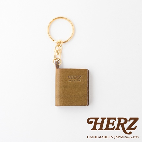 職人手作皮革書本造型鑰匙圈，採用棕色皮革製作，表面壓印「HERZ」及「MADE IN JAPAN」字樣，搭配金色鑰匙圈。