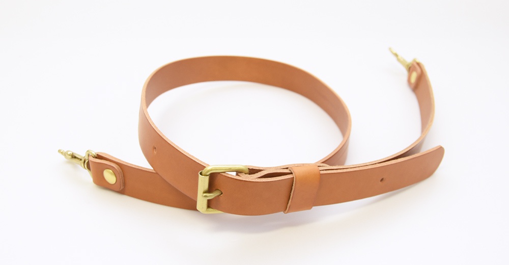 一條棕褐色皮革製成的肩背帶，帶有黃銅色金屬扣環和掛鉤。