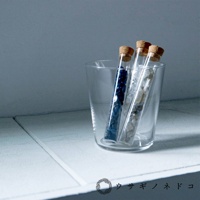 玻璃杯中裝有三個帶軟木塞的試管，試管內分別裝有藍色小顆粒、米白色和灰色碎石。