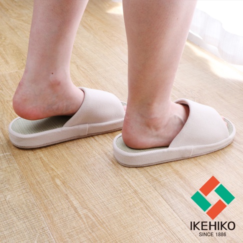 一雙淺米色藺草透氣室內拖鞋，鞋面為織紋材質，鞋底為藺草編織，展示於木質地板上。