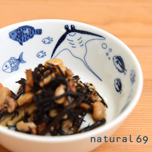 白色陶瓷小碗內盛裝著黑色海帶、豆子及少量橘色配料，碗內壁繪有藍色線條的海底動物圖案，包括魚群和一隻魟魚。