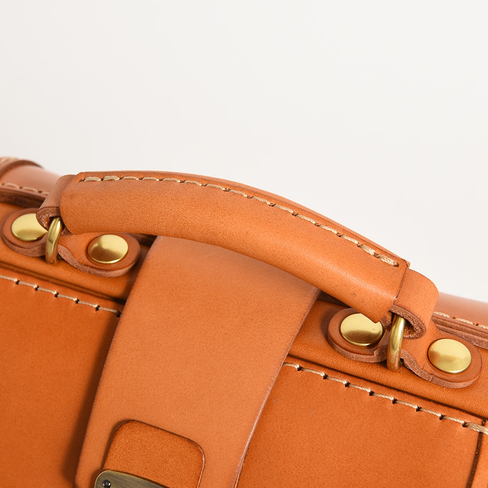 焦糖色皮革迷你後背醫生包，特寫手提把與金屬旋鈕，展現職人細膩手縫工藝。
