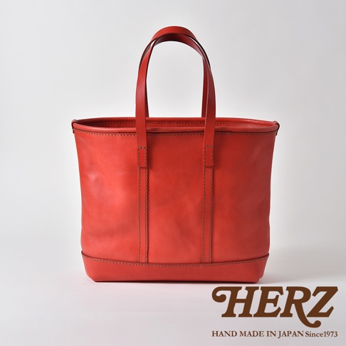 紅色皮革經典托特包，方形包身，雙提把設計，簡約縫線，底部加固，質感皮革，品牌標誌在右下角。