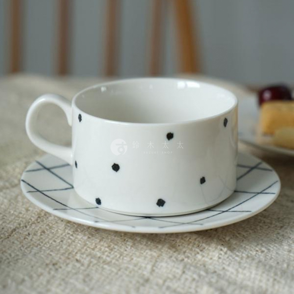 白色陶瓷咖啡杯，點綴黑色手繪圓點，搭配同系列棋盤格圖案的白色陶瓷杯墊。