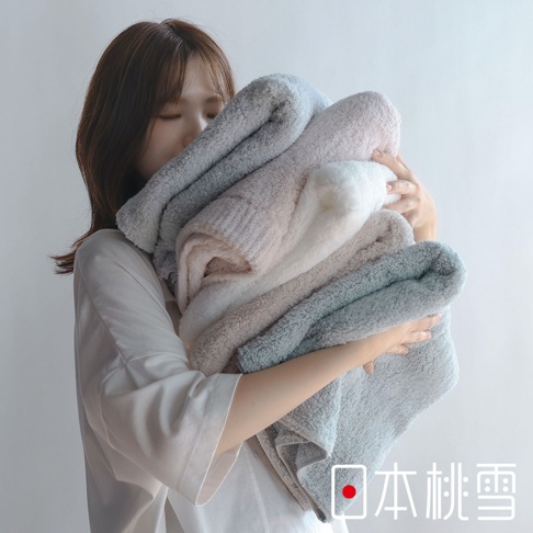 日本桃雪品牌標誌旁，一名女子懷抱著一疊柔軟蓬鬆的毛巾，毛巾顏色從淺灰到白色、米色，再到淺藍色，營造出溫馨舒適的氛圍。