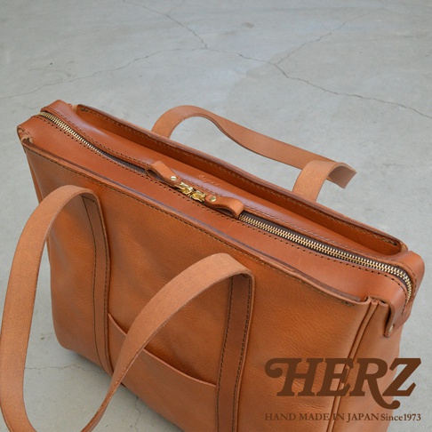 職人手作皮革Organ肩背拉鍊托特包，採用天然棕色皮革製成，配有黃銅色拉鍊和皮革提把。包身線條簡潔，展現皮革的質感。