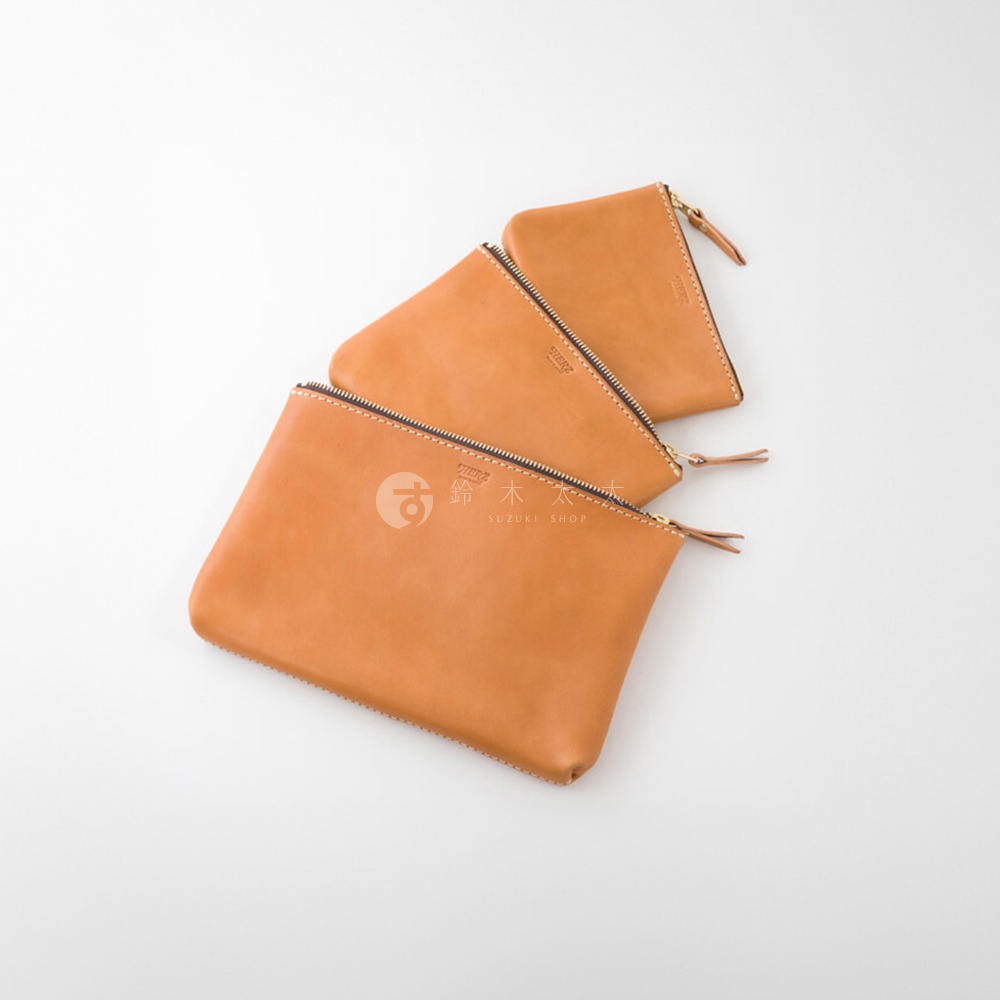 三個棕褐色皮革長方形拉鍊收納包，由淺至深堆疊，皮質光滑，配有金色拉鍊及同色皮革拉頭，其中兩個包的拉鍊處印有品牌標誌。