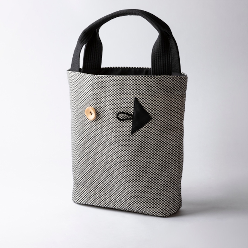三河木綿刺子織直式收納托特包，以黑白格紋布料製成，配有黑色提把，包身正面有一個木質鈕扣與黑色箭頭造型裝飾。