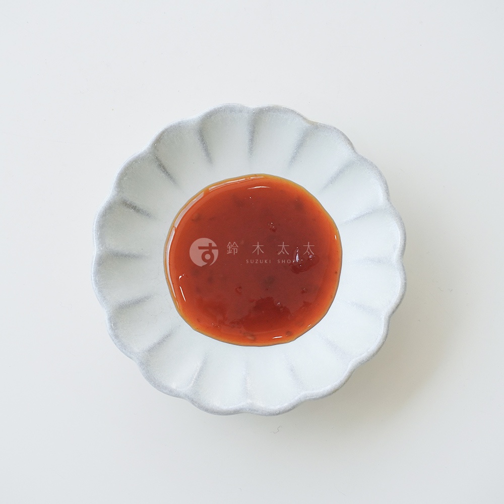 頂部視角下，一個淺灰色花瓣形狀的醬料碟中盛有紅棕色醬料，醬料中央印有「鈴木太太 SUZUKI SHOP」的文字和圖標。