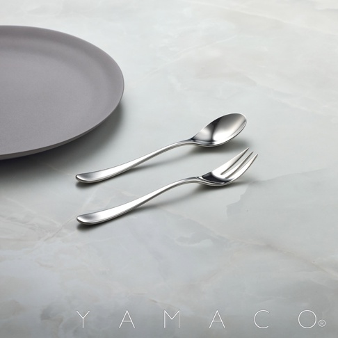 一個霧面不鏽鋼點心叉匙組，以及一個同色系的圓盤，擺放在大理石紋的桌面。