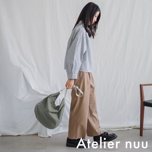 Atelier nuu 模特手提著淺綠色斜背包，身穿條紋襯衫和卡其色寬褲