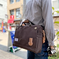 深棕色純棉帆布製成的B4商務公事包，配有皮革提把與裝飾。包款外側有一個翻蓋口袋，上面有皮革裝飾片，側邊掛有皮革吊牌。