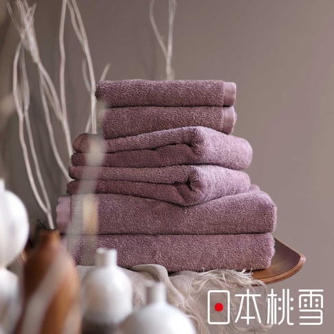 堆疊的精梳棉飯店毛巾，呈現柔和的紫羅蘭色，毛圈蓬鬆，質感細膩。