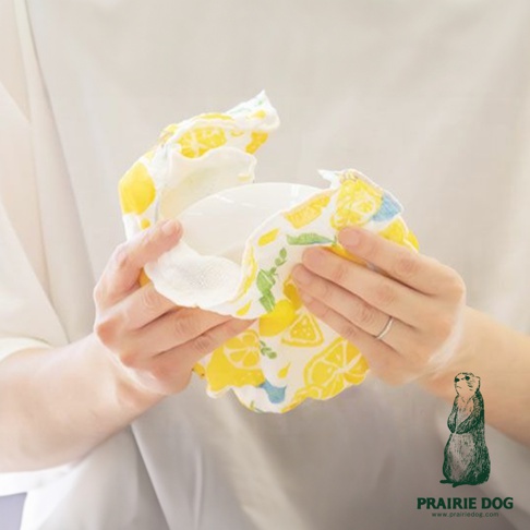 一條黃色檸檬圖案的五層紗質地擦拭巾，被雙手包裹著一個白色碗，展示其吸水性。