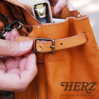 職人手作皮革水洗加工復古郵差包，採用棕色皮革，配有黃銅色金屬扣環和鉤環，展示其細節和質感。