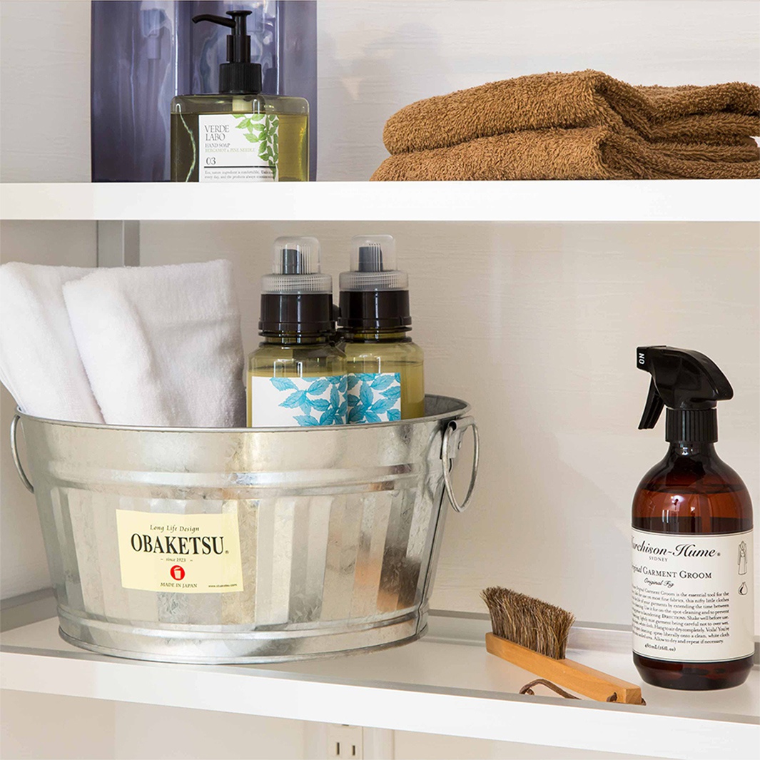 木製手柄的刷子、帶有標籤的灰色金屬桶，裡面裝有毛巾和兩個噴霧瓶，以及一個帶有標籤的深棕色噴霧瓶。