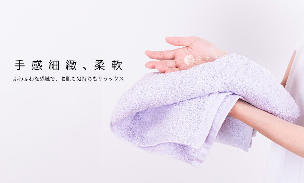 一條淺紫色毛巾，材質柔軟，紋理清晰，被一隻手握住，展示其質地。